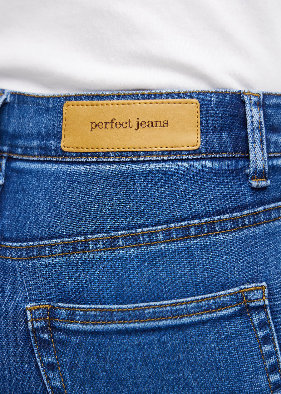 Close-up of dark blue denim with the Perfect Jeans logo label at the edge of the front pocket.