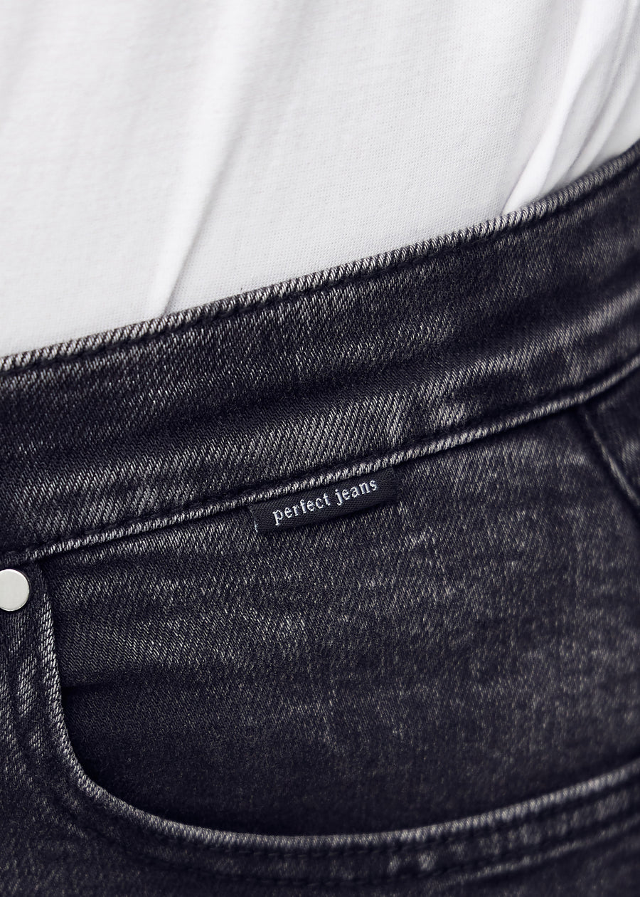 Close-up of dark grey denim with the Perfect Jeans logo label at the edge of the front pocket.