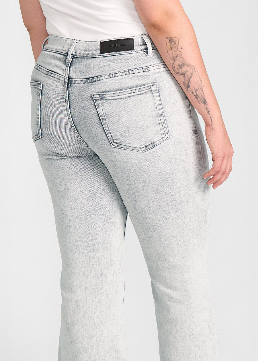 Lysegrå denim bootcut jeans, modelnavn Ashes, som sidder tæt om hofter og lår med et let svaj fra knæet og ned, set bagfra tæt på for at vise detaljer. på en plus-size model.