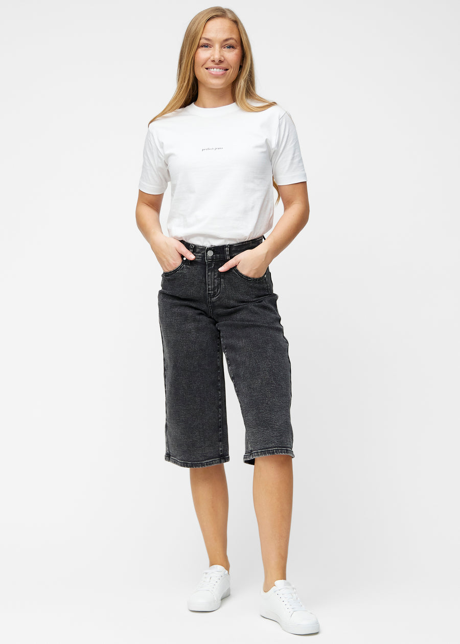 Fuldt billede af model i løse, mørkegrå denim capris i farven Shadows, der går til lige under knæet.