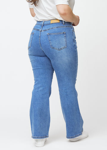 Blue mid-rise bootcut jeans in Rivers. Back view on a plus-size model, showing the full fit.