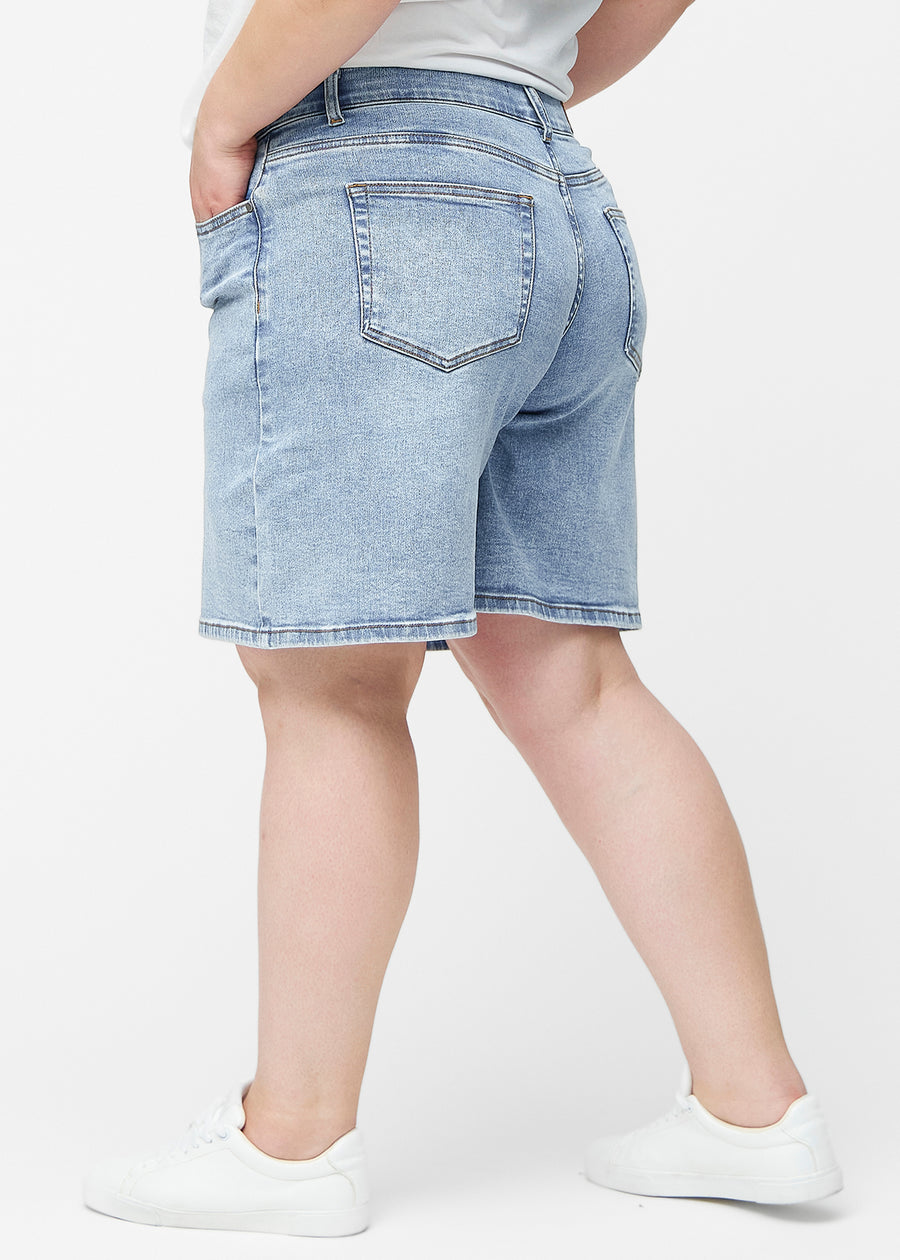 Plus-size model stretches the loose, light blue denim shorts in the colour Waves at the hips to show the material’s stretch.