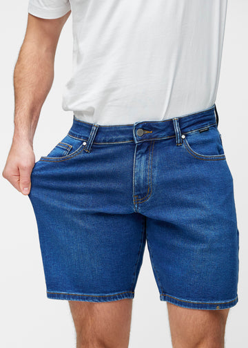 Model stretches the dark blue denim shorts for men in the colour Oceans at the thigh to show the stretch of the material.