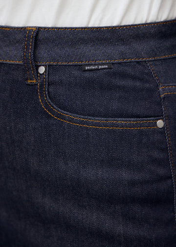 Close-up of deep dark blue denim with Perfect Jeans logo label at the front pocket edge on a plus-size model.