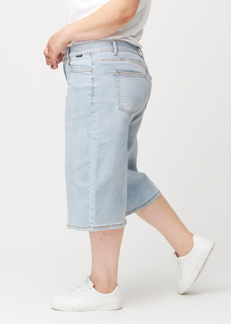 Løse, lyseblå denim capris i farven Waves set fra siden på plus-size model, hvor den brede pasform og længden til lige under knæet er synlig.
