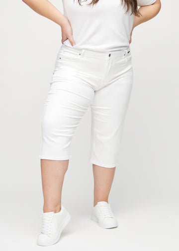 White regular capris, model name Marguerites, which have a straight fit through the leg and end just below the knee on a plus-size model, seen from the front.