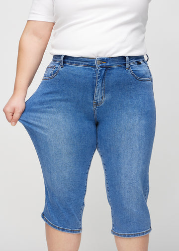 The plus-size model stretches the capris at the thigh to show the stretch.