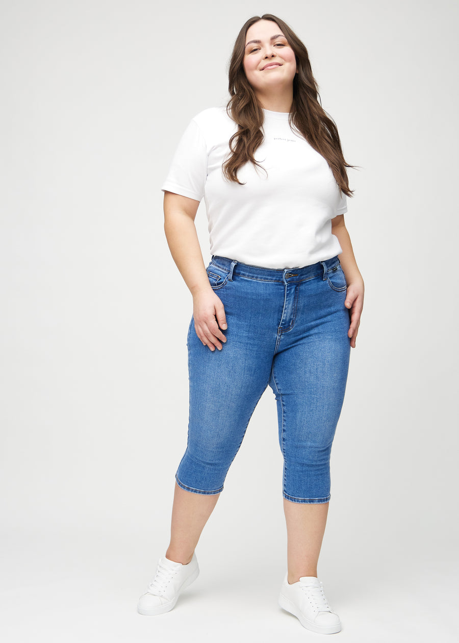 Skinny capris for women in blue denim, color Rivers. Full-length view of a plus-size model wearing the capris.