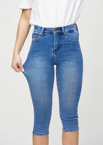 Skinny capris for women in blue denim, color Rivers. A model stretches the fabric to demonstrate its flexibility.