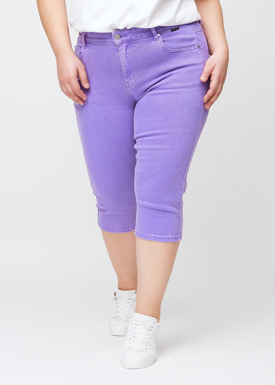 Slim capris for women in pastel purple jeans fabric, color Lavenders. Front view on a plus-size model, showing the fitted cut ending just below the knee.