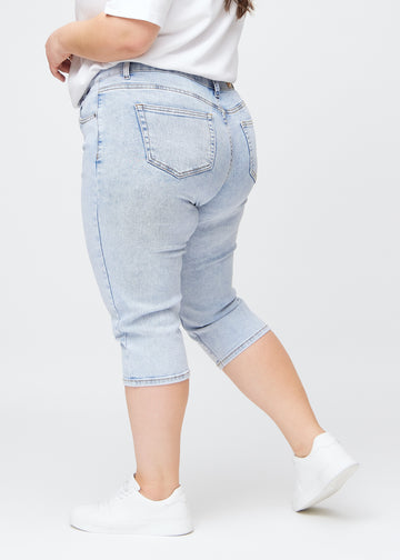 Slim capris for women in light blue denim, color Waves. Side view on a plus-size model, showing the tailored fit and mid-rise waist.