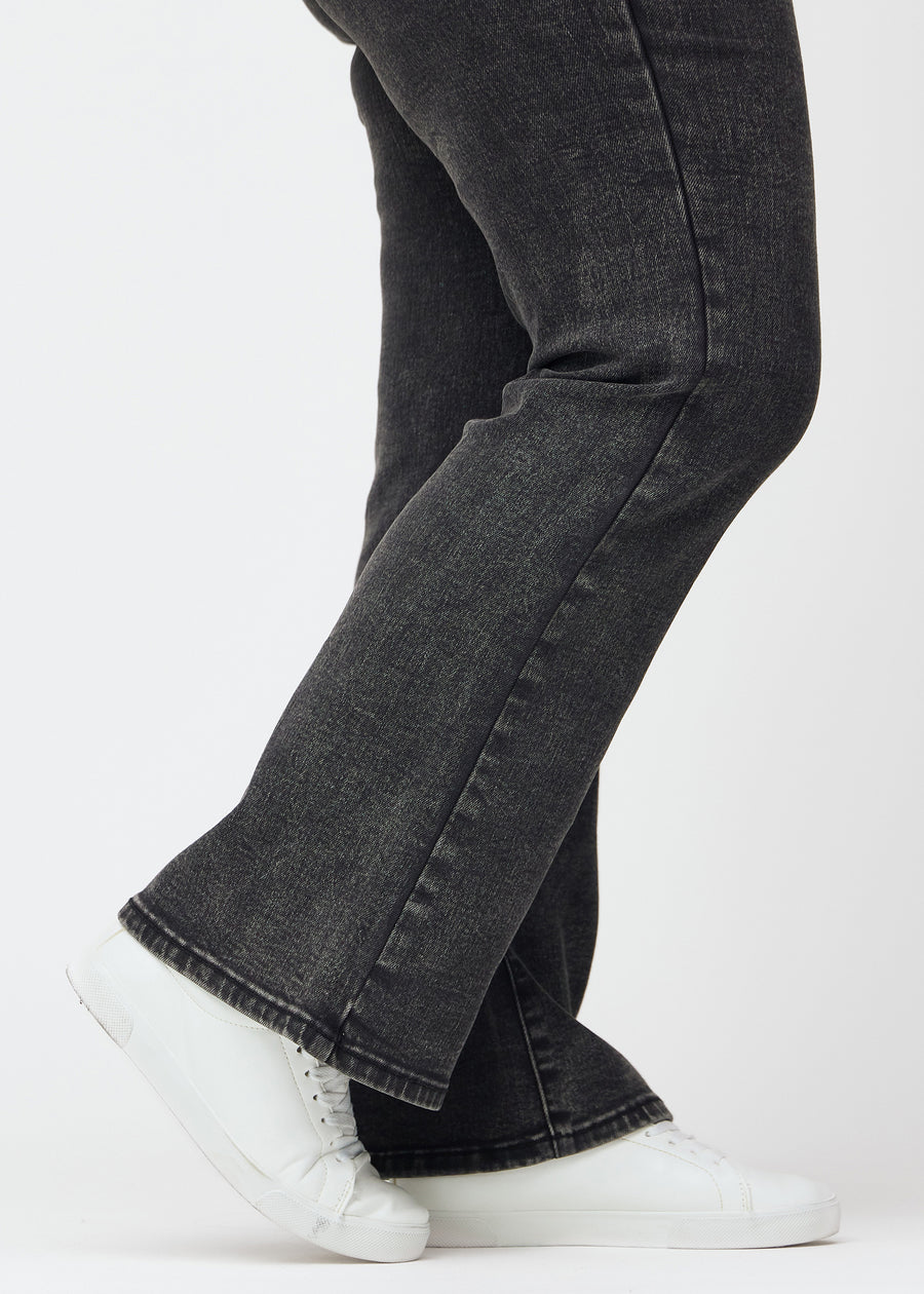 Dark grey mid-rise bootcut jeans in Shadows. Close-up of the ankle area on a plus-size model, showing the subtle bootcut flare.