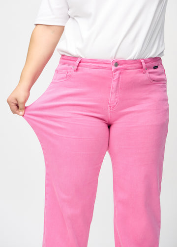 Loose jeans for women in light pink, color Flamingos. A plus-size model stretches the denim at the thigh to show the fabric&