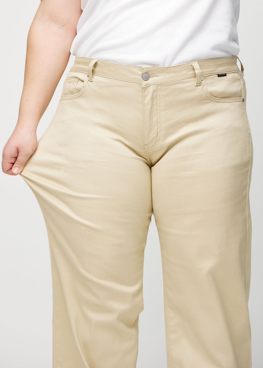 Loose jeans for women in beige, color Gazelles. A plus-size model stretches the denim at the thigh to show the fabric&