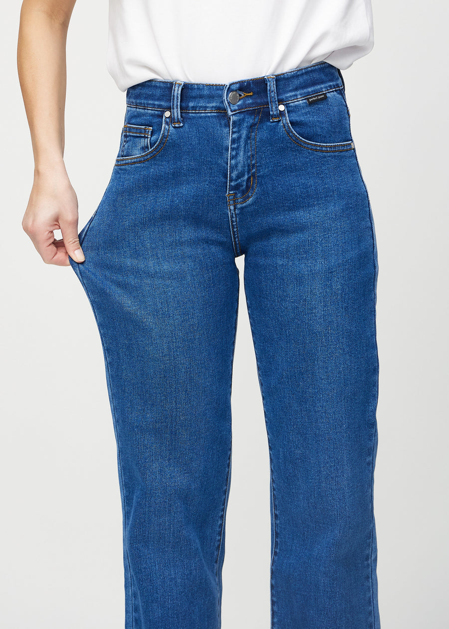 Loose jeans for women in dark blue, color Oceans. A model stretches the denim at the thigh to show the fabric&