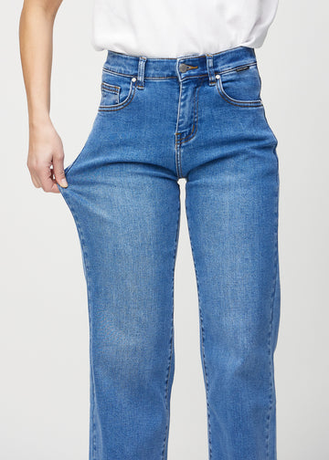 Loose jeans for women in blue, color Rivers. A model stretches the denim at the thigh to show the fabric&