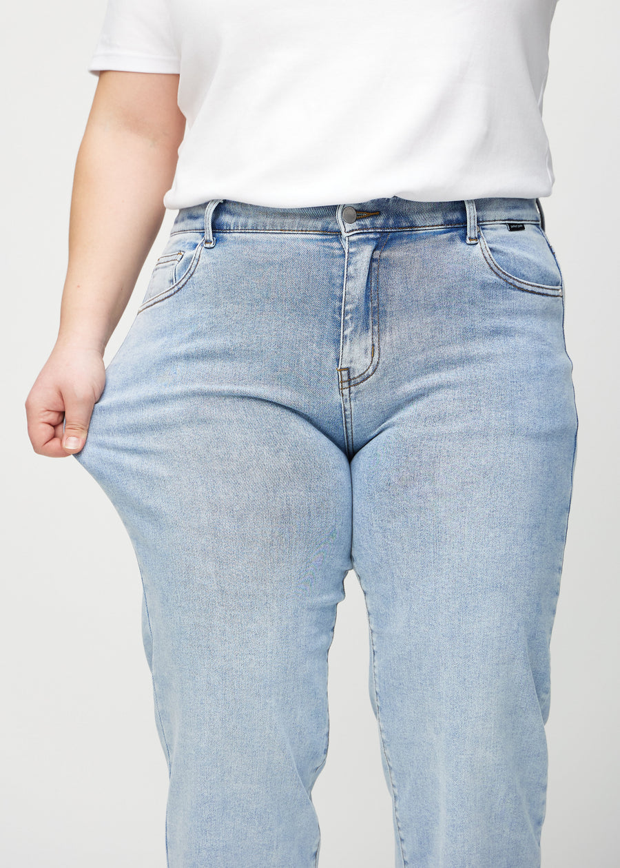 The plus-size model stretches the jeans at the thigh to show the stretch.