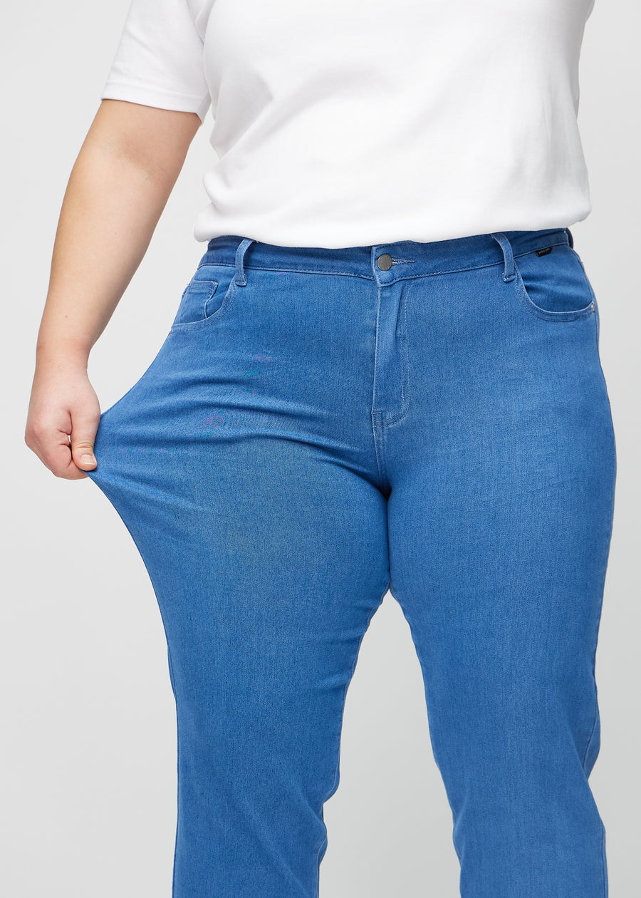 Regular jeans for women in blue, color Geraniums. A plus-size model stretches the fabric at the thigh to show its stretch.