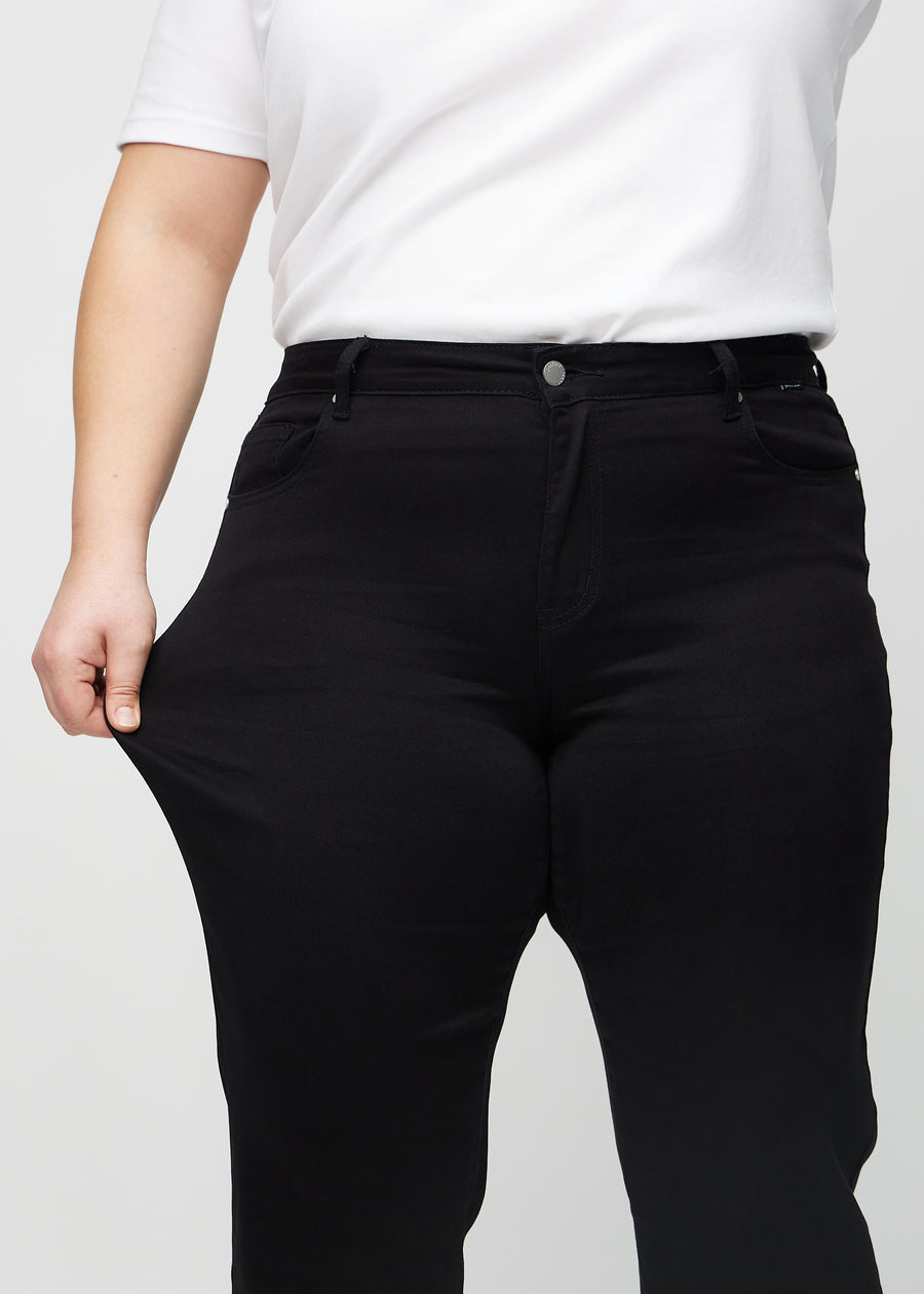 The plus-size model stretches the jeans at the thigh to show the stretch.