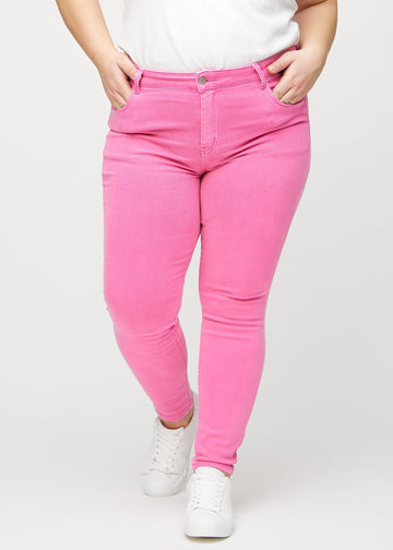 Skinny jeans for women in light pink, color Flamingos. Front view on a plus-size model, showing the close fit through the legs.