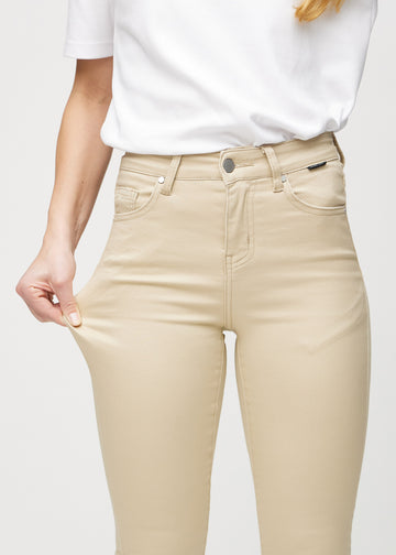 Skinny jeans for women in beige, color Gazelles. A model stretches the jeans at the thigh to show the fabric&