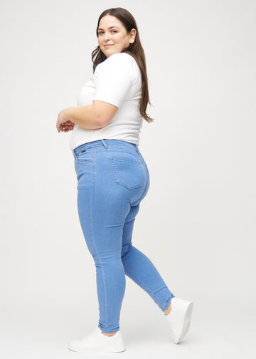 Blue skinny jeans seen from the side on a plus-size model.