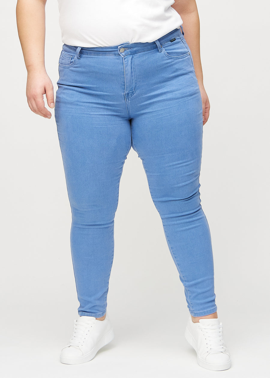 Blue skinny jeans, model name Geraniums, which fits closely to the leg on a plus-size model, seen from the front.