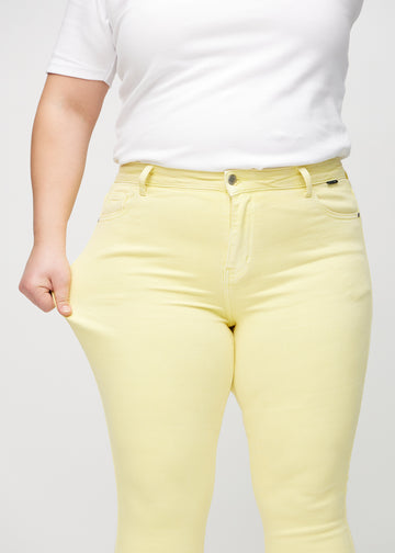 Skinny jeans for women in light yellow, color Lemonades. A plus-size model stretches the jeans at the thigh to show the fabric&