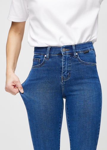 Skinny jeans for women in dark blue, color Oceans. A model stretches the jeans at the thigh to show the fabric&
