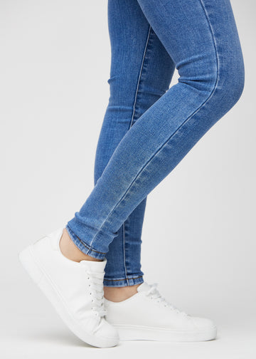 Skinny jeans for women in blue, color Rivers. Close-up of the snug-fitting leg openings at the ankles on a model.