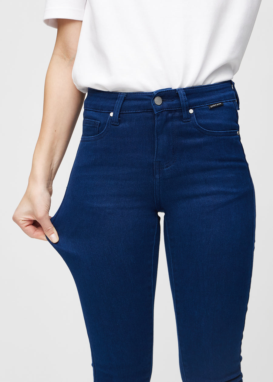 Skinny jeans for women in dark blue, color Royals. A model stretches the jeans at the thigh to show the fabric&