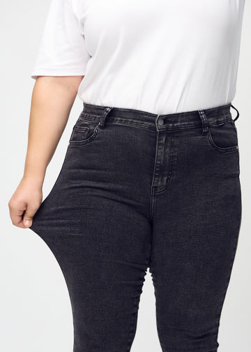 Skinny jeans for women in dark grey, color Shadows. A plus-size model stretches the jeans at the thigh to show the fabric&