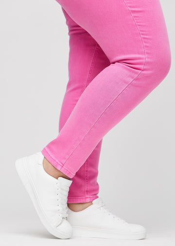 Slim jeans for women in light pink, color Flamingos. Close-up at the ankles on a plus-size model, showing the fit at the leg openings.