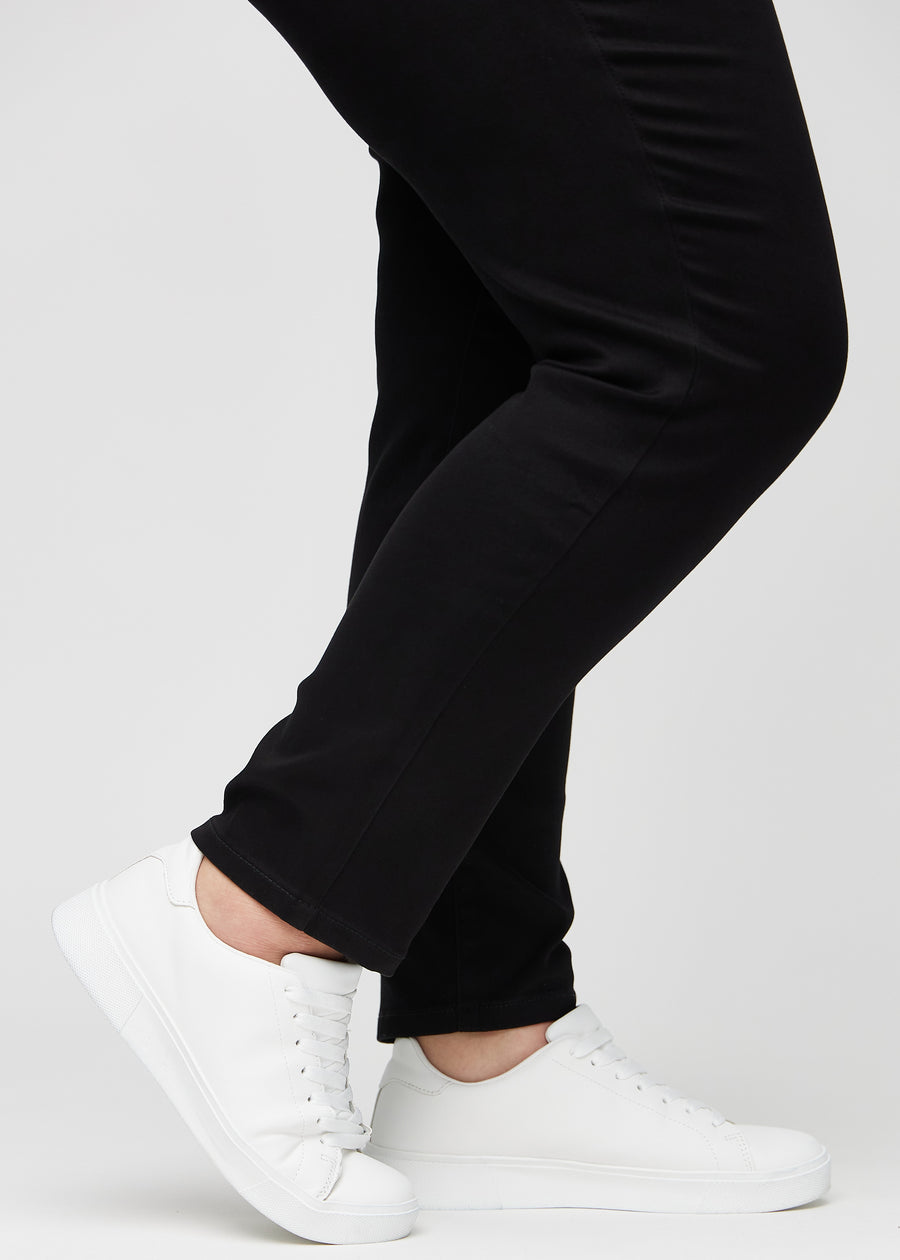 Slim jeans for women in black, color Ravens. Close-up at the ankles on a plus-size model, showing the fit at the leg openings.