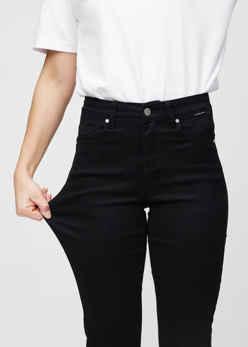 Slim jeans for women in black, color Ravens. A model stretches the jeans at the thigh to show the fabric&