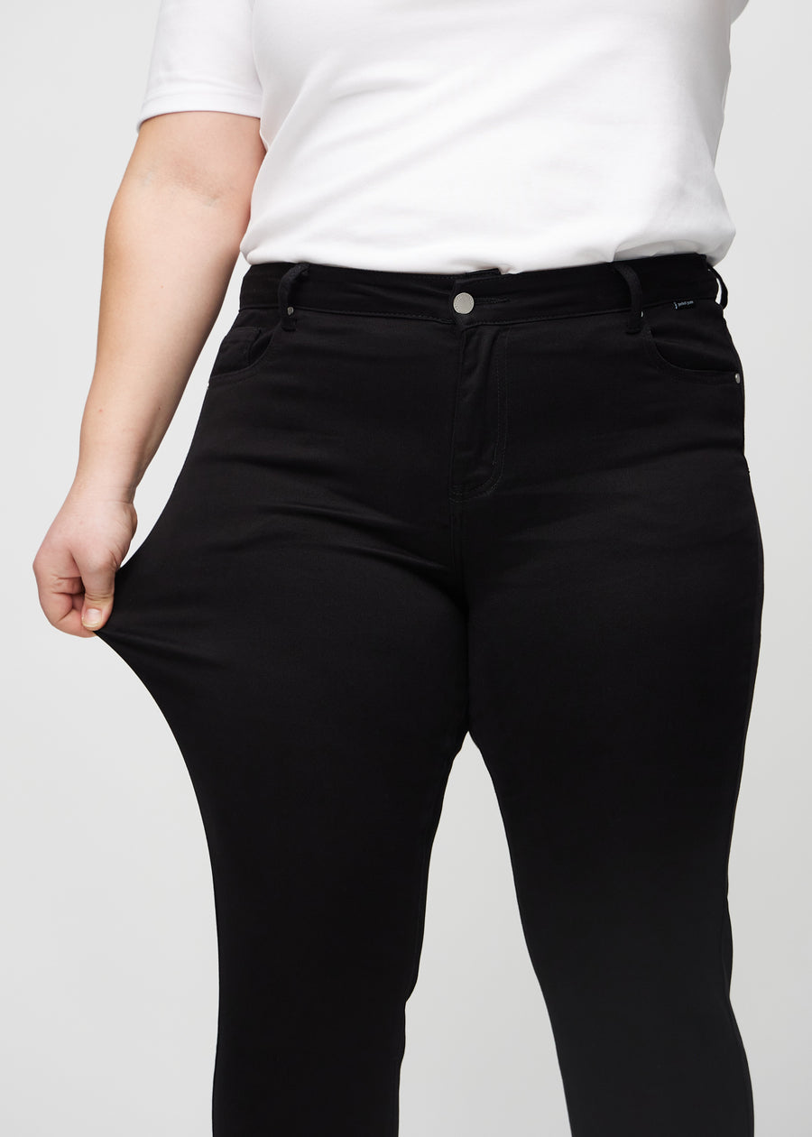 Slim jeans for women in black, color Ravens. A plus-size model stretches the jeans at the thigh to show the fabric&