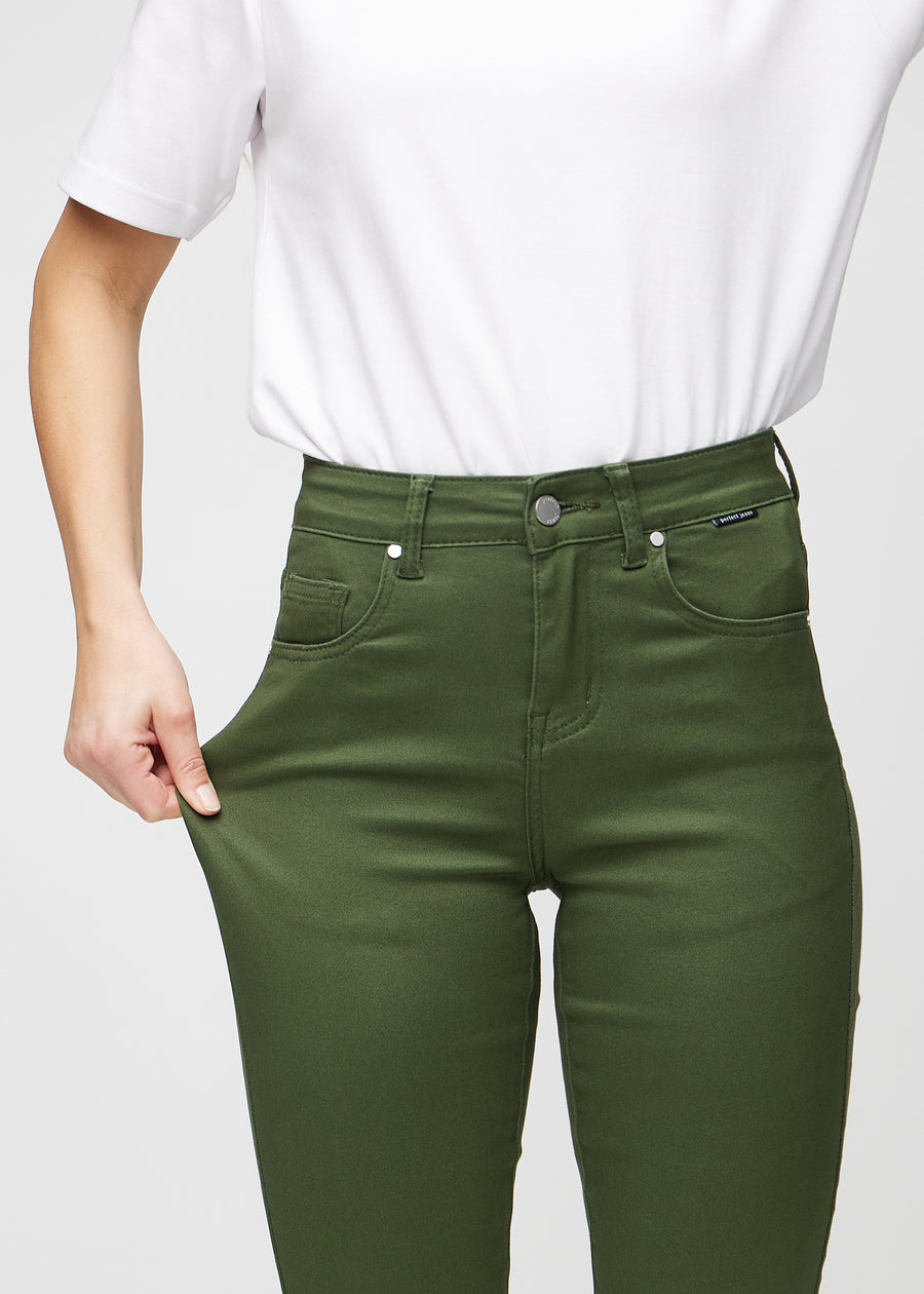 Slim jeans for women in dark green, color Renewals. A model stretches the jeans at the thigh to show the fabric&