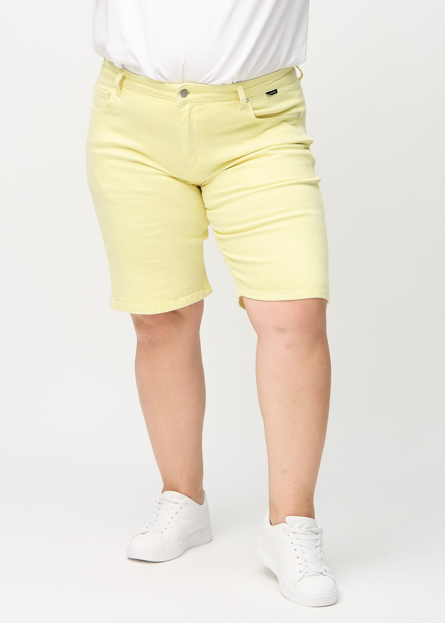 Light yellow regular middle shorts, model name Lemonades, which fall straight down the leg and end just above the knee on a plus-size model, seen from the front.
