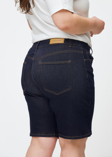 Deep dark blue denim shorts for women in the colour Midnights seen from the back in close-up on a plus-size model.