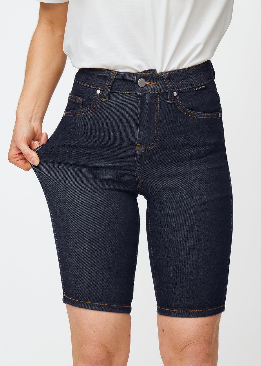 Model stretches deep dark blue denim shorts for women in the colour Midnights at the thigh to show the material’s stretch.