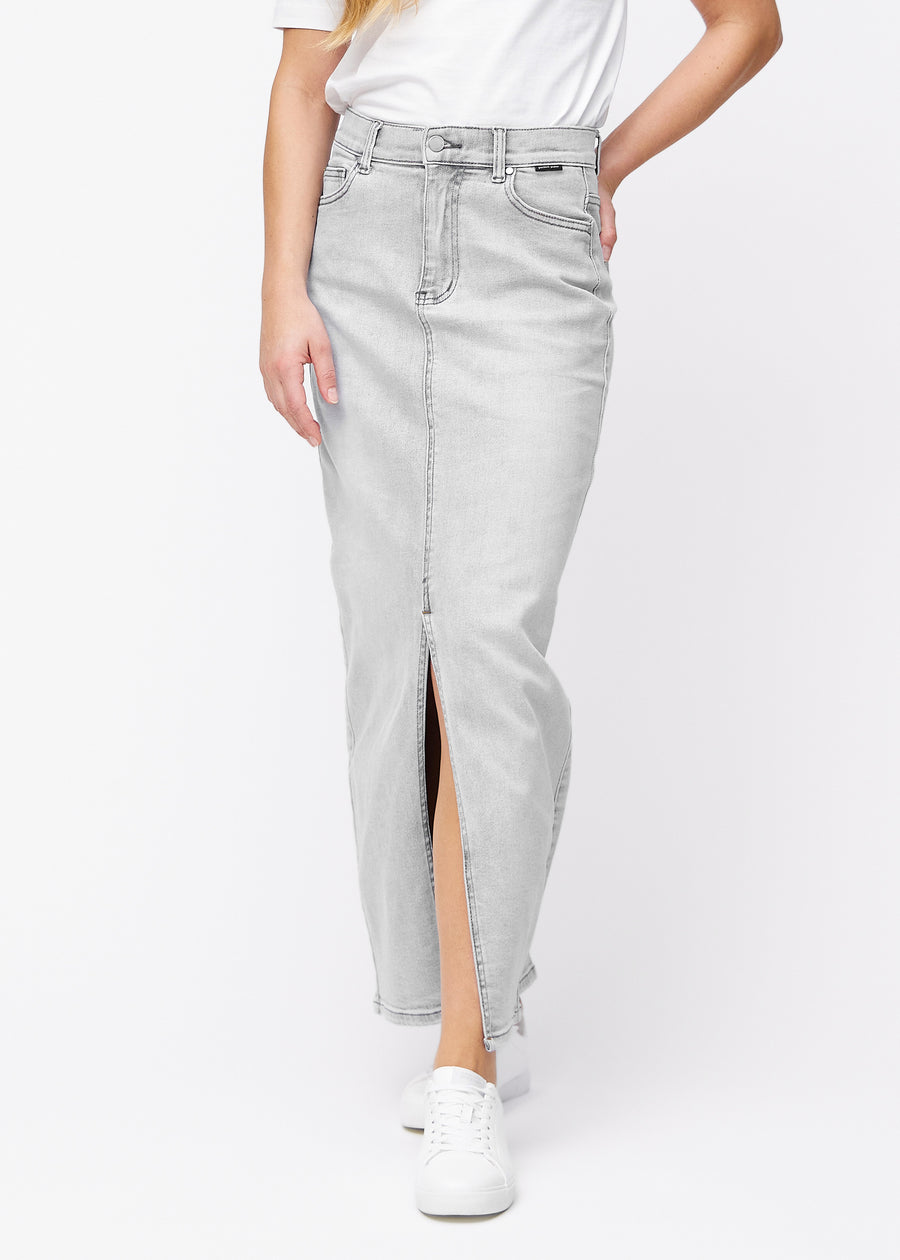 Long light grey denim skirt for women in the color Ashes. Front view on a model, showing the straight fit from the hips and a front slit starting below the knee.