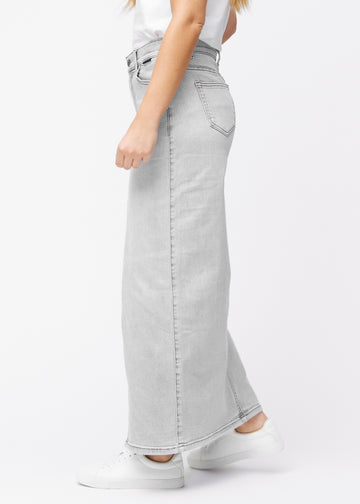 Long light grey denim skirt for women in the color Ashes. Side view on a model, with the front slit visible.
