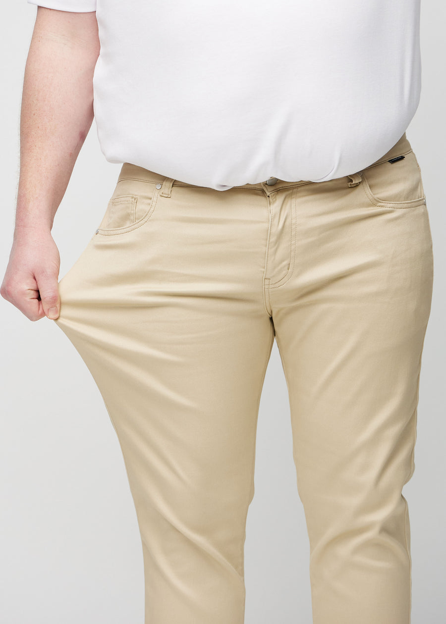 Plus-size model strækker jeansene ved låret for at vise stretch.