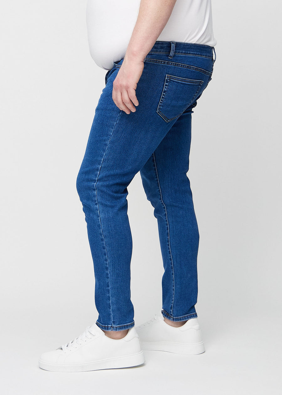 Dark blue denim slim jeans viewed from the side on a plus-size model.