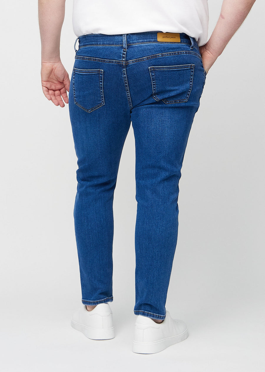 Dark blue denim slim jeans viewed from the back on a plus-size model to show the full product.
