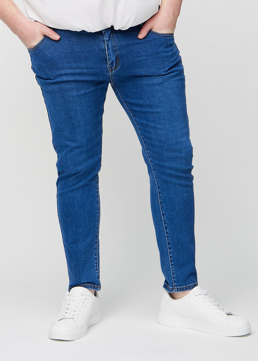 Dark blue denim slim jeans, model name Oceans, fitted closely along the legs on a plus-size model, front view.