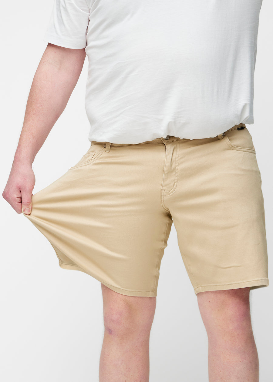 Plus-size model stretches the beige shorts for men in the colour Gazelles at the thigh to show the stretch of the material.