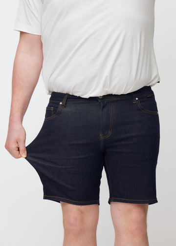 Plus-size model stretches deep dark blue denim shorts for men in the colour Midnights at the thigh to show stretch.