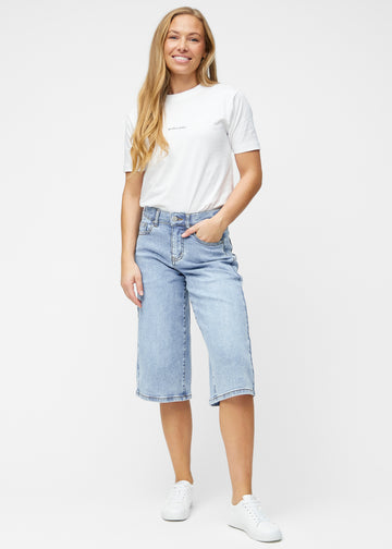 Model viser løse, lyseblå denim capris i farven Waves i bevægelse og demonstrerer pasform og materiale.