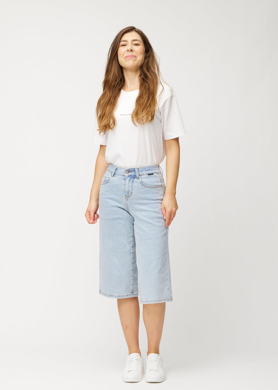 Model viser løse, lyseblå denim capris i farven Waves i bevægelse og demonstrerer pasform og materiale.
